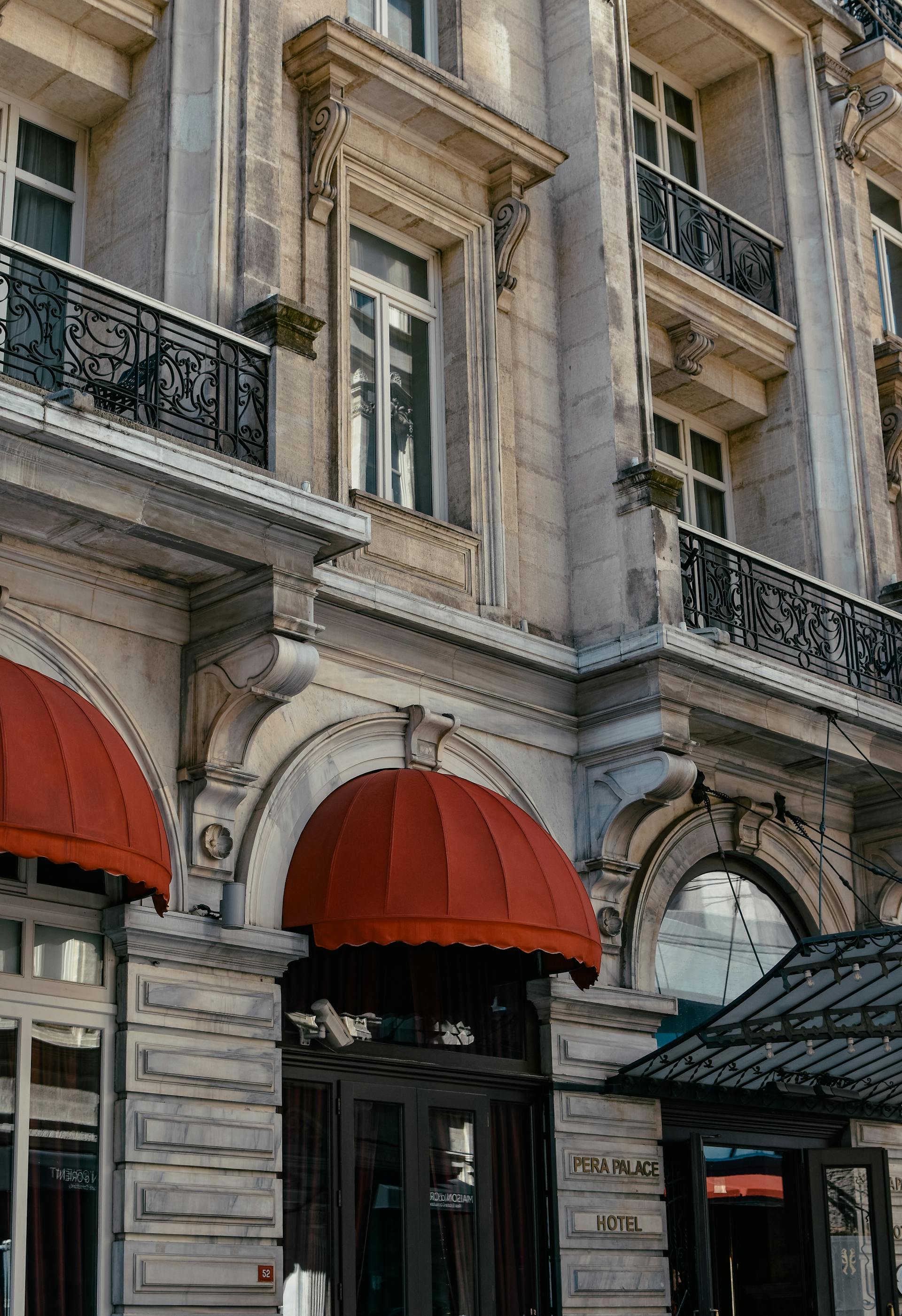 Classical stone hotel facade with arched entrances and red awnings, evoking refined hospitality